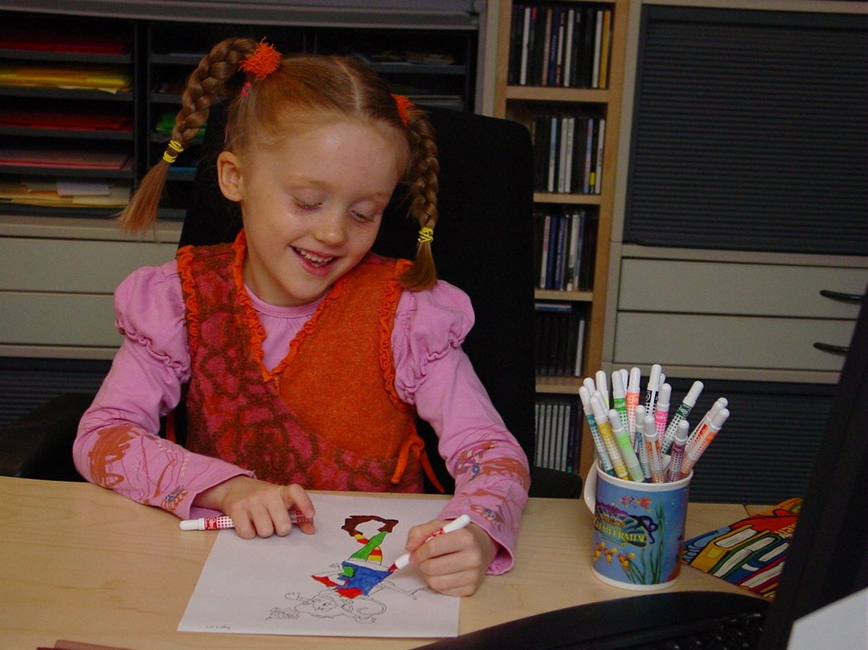 Ilse as a young child, colouring in a drawing at a desk full of markers
